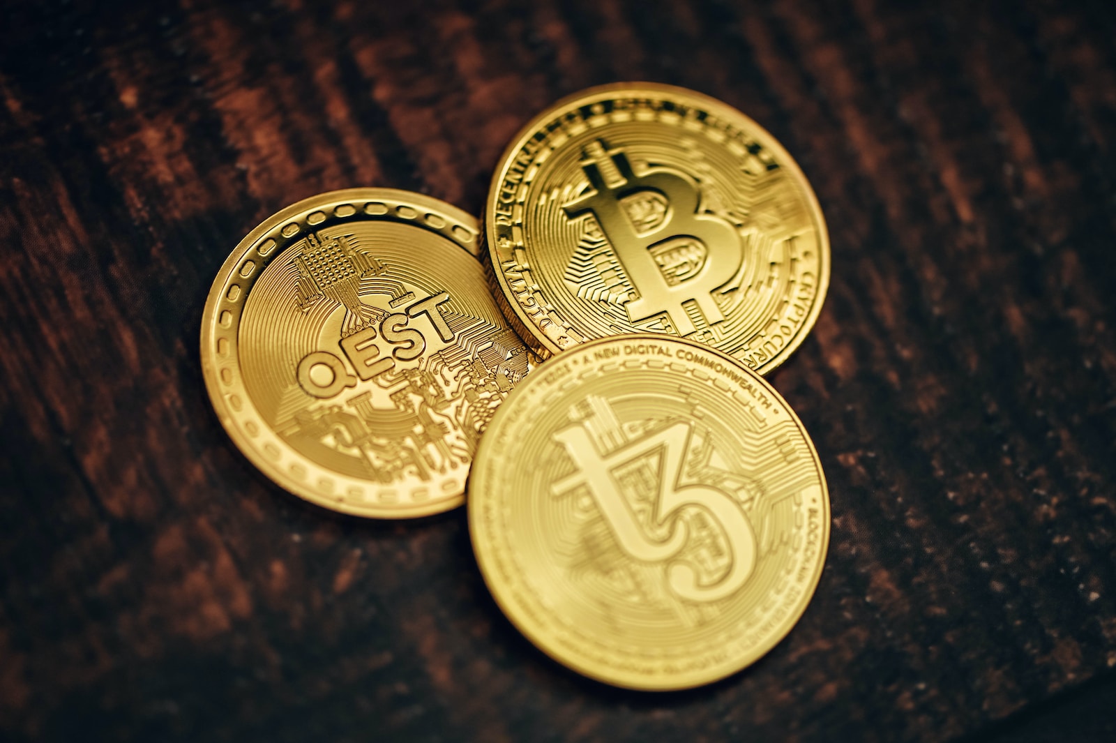 three gold bitcoins sitting on top of a wooden table